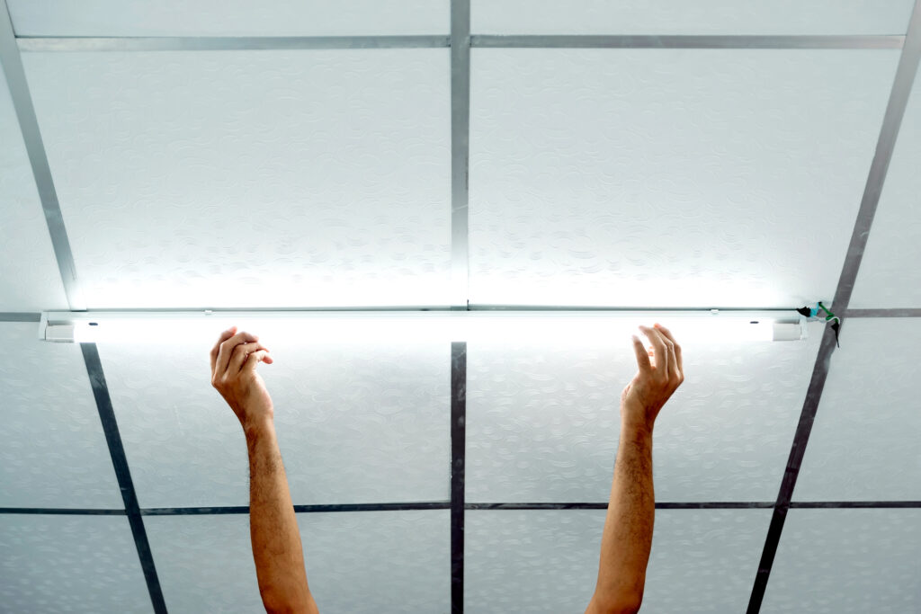 Close-up of a man's hand installing a long LED light bulb on the ceiling. Image credit: iStock
