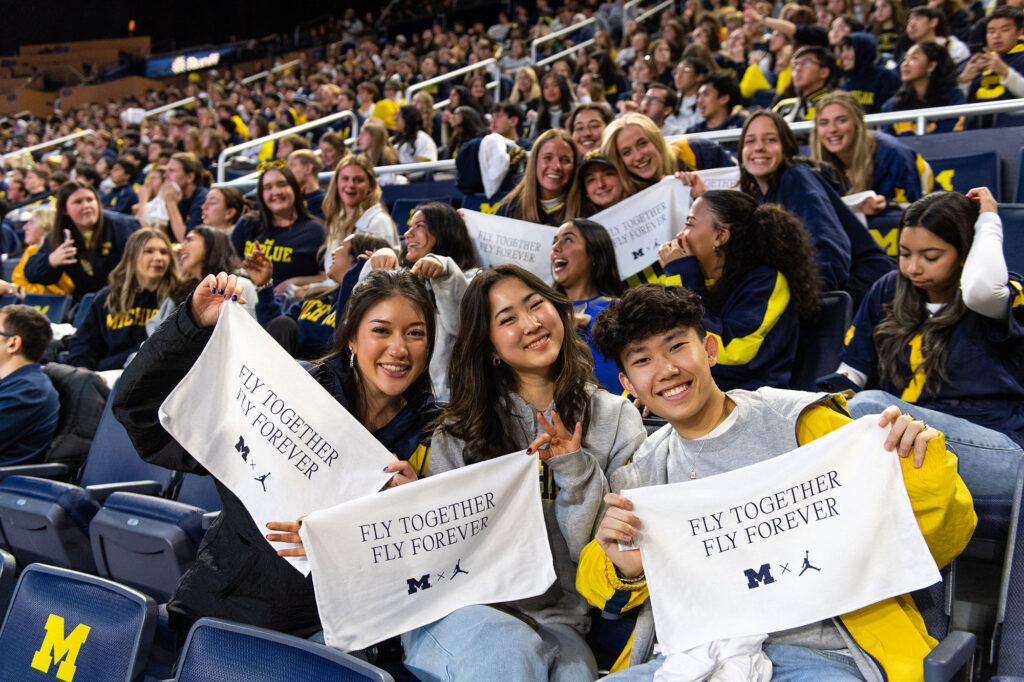 Photo ofstudents displaying souvenir towels during a watch party at Crisler Center.