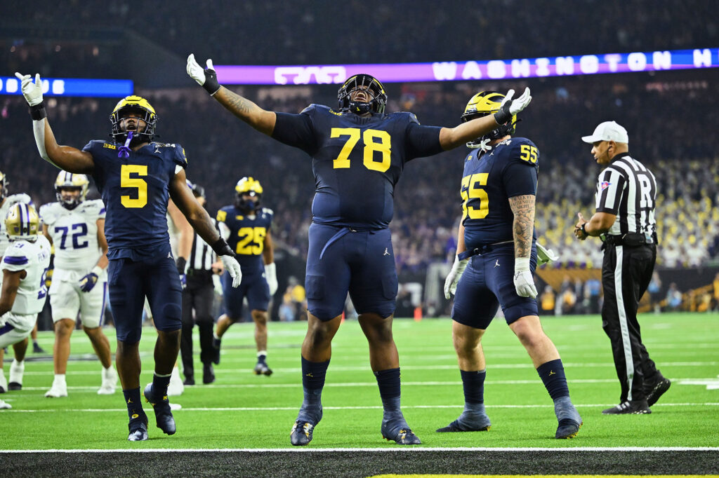 Photo of Wolverines Josaiah Stewart,  Kenneth Grant and Mason Graham celebrating a big defensive play.