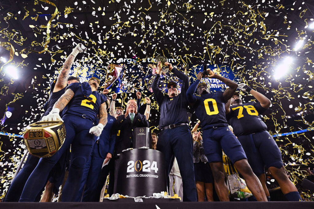 Photo of head coach Jim Harbaugh, surrounded by his players, holding the national championship trophy.