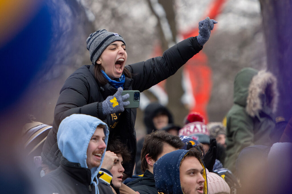 A fan shows their enthusiasm from the shoulders of another parade watcher.