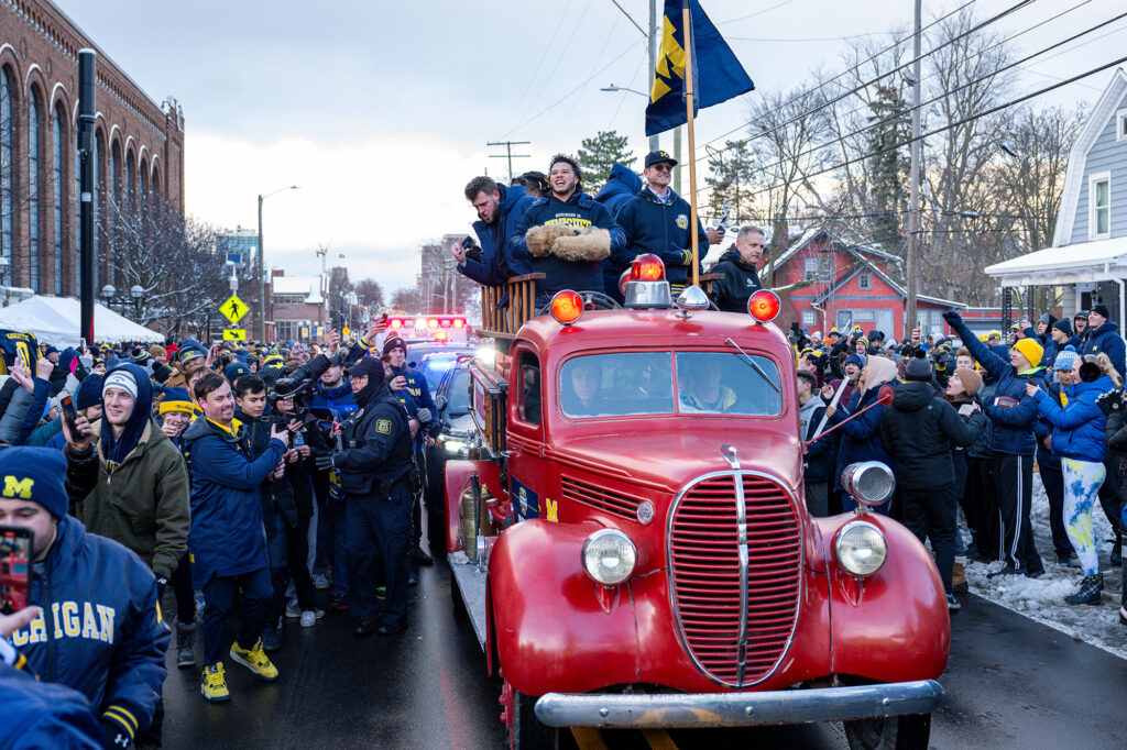 Team members celebrate with the crowd as the antique firetruck they were riding passes Yost Ice Arena. 