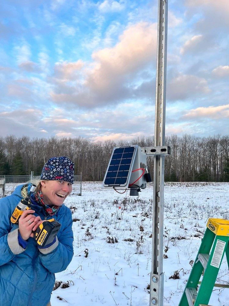 A photo of a woman by a sensor that measures snowpack