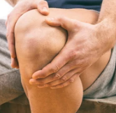 A caucasian person touches their knee, which appears to be in pain.