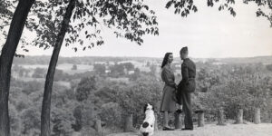 A World War II-era couple in black & white image overlooking a tree-covered valley.