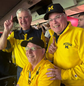 Three older caucasian men dressed in maize with blue M caps.