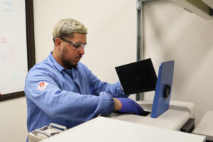 Figueroa Morales has a gloved hand inside the spectrometer, which looks like a large, tan box with a blue, hinged lid.
