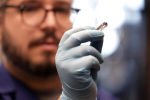 Pena-Francesch holds up a transparent, pill-shaped capsule in a gloved hand.
