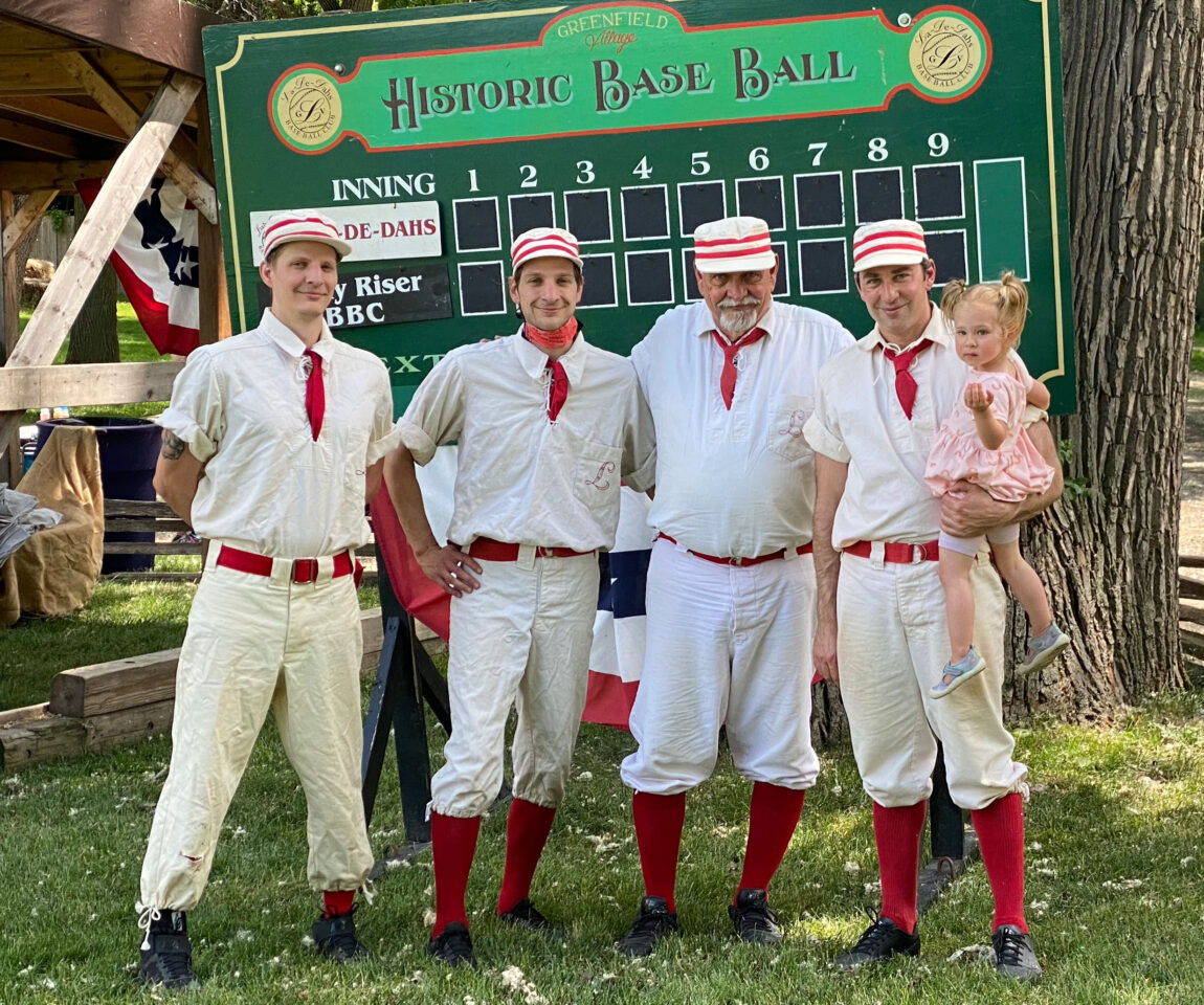 A photo of four men wearing old baseball uniforms, one holding a small child