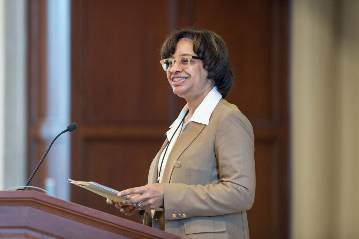 A photo of a woman standing and smiling at a podium