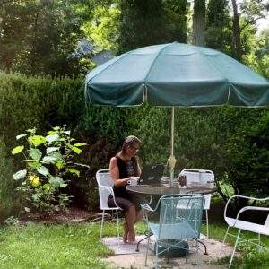 Woman works on laptop at an outdoor patio table surrounded by greenery.