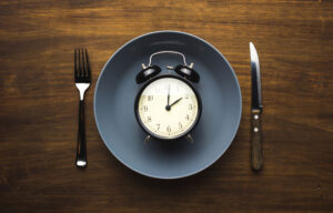 An old-fashioned alarm clock sits atop a plate as a metaphor for intermittent fasting.