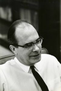 Black and white photo of balding caucasian man with glasses, white shirt, and tie, circa 1970.