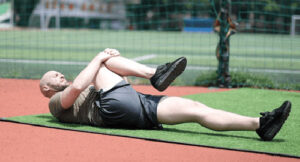 Person lies on the ground on their back, pulling one knee toward upper body using both hands.