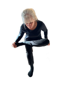 Person sits as though in a char with one leg crossed over the other, holding foot