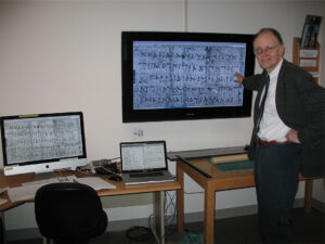 Man stands at monitor showing ancient language on a scroll dating to 