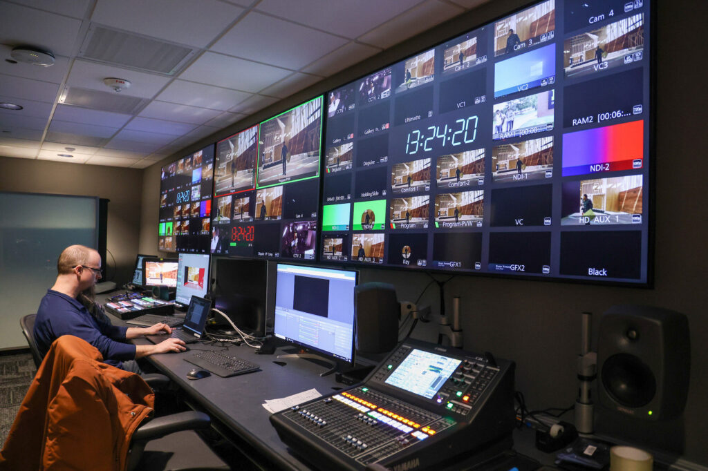 Man sits in editing bay with several color monitors, like a control room.