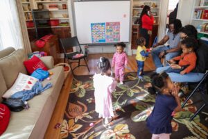 Toddlers play together in a colorful living room while parents look on.