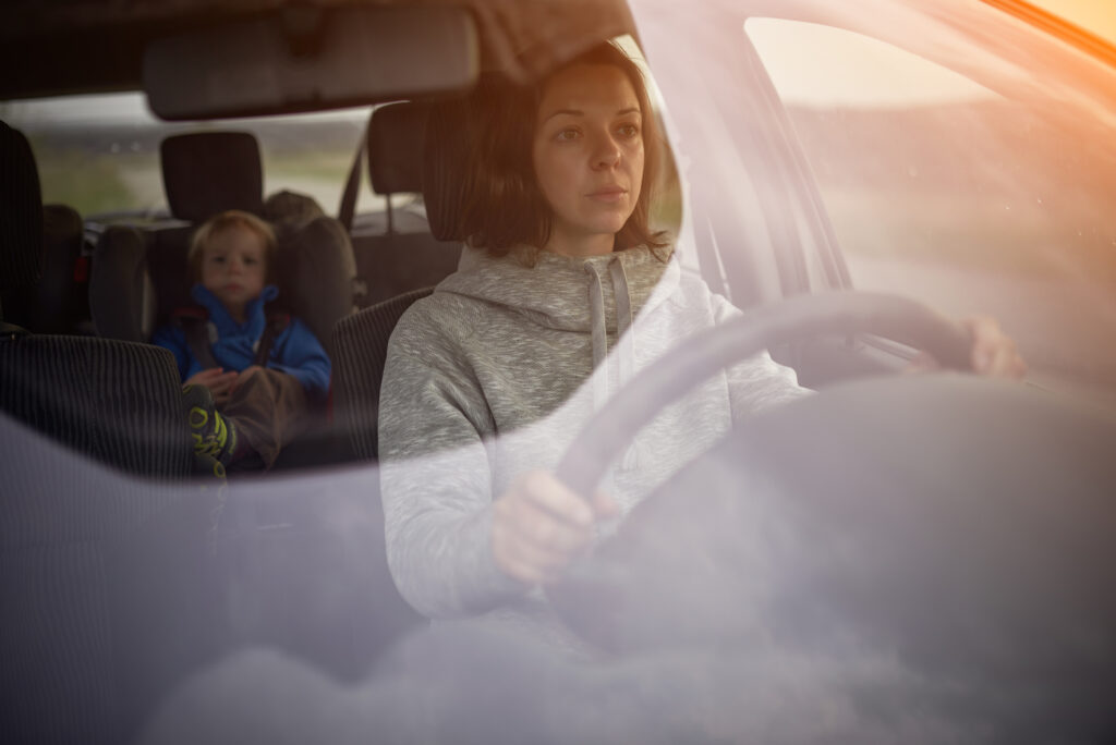 Mother drives a car, a child in a safety seat in the rear seat. Image credit: iStock