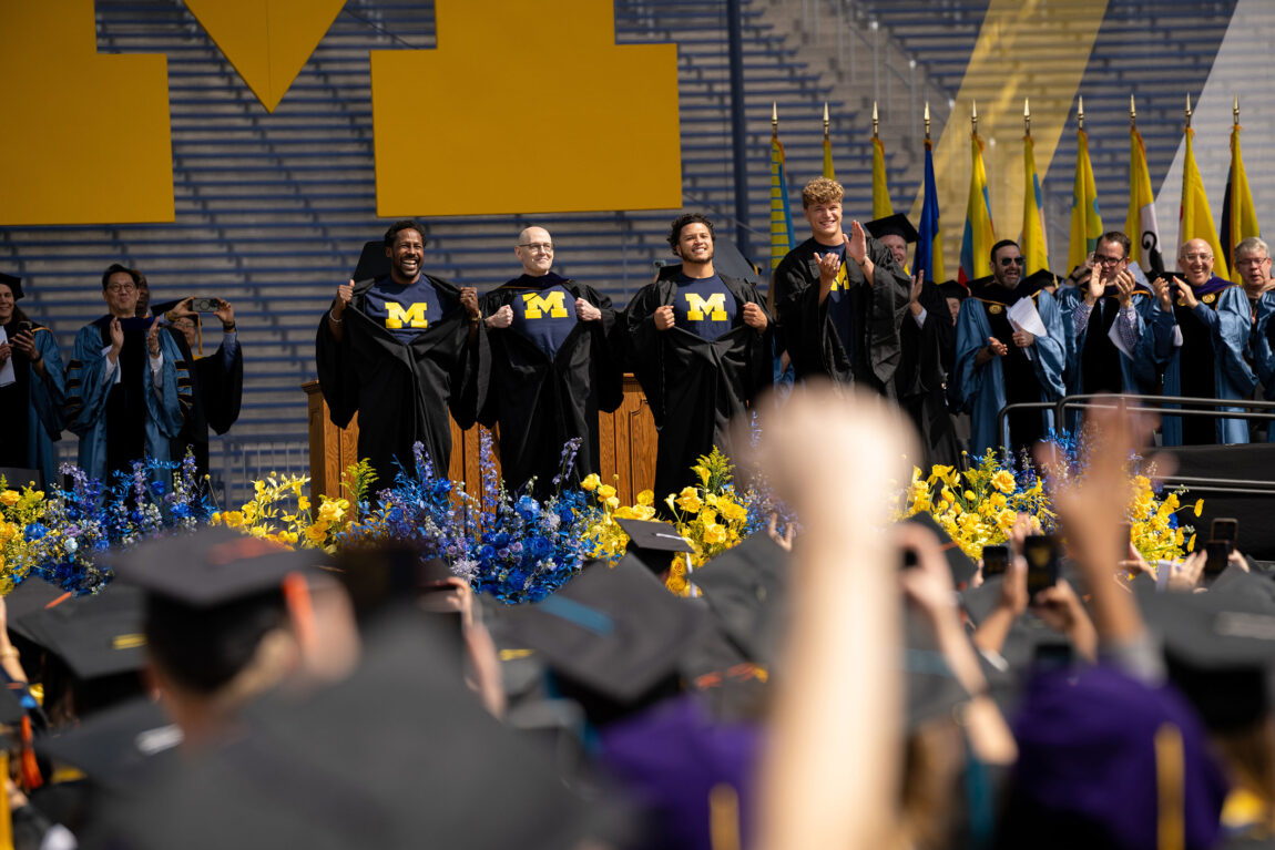 Desmond Howard, Brad Meltzer, Blake Corum and J.J. McCarthy reveal shirts bearing the Block M from under their gowns
