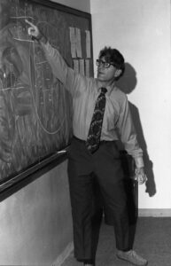 Black and white image of professor pointing to chalk board.