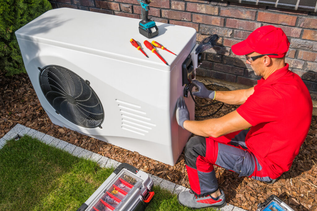 Professional Middle Aged HVAC Technician in Red Uniform Repairing Modern Heat Pump Unit. House Heating and Cooling System Theme. Image credit: welcomia, iStock