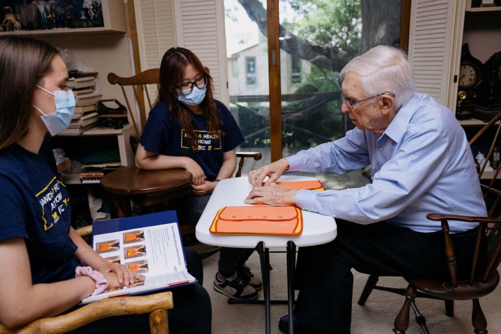 Two master's students observe as a Hands and Health at Home participant practices buttoning on a sample button board. Image credit: Erin Kirkland, Michigan Photography