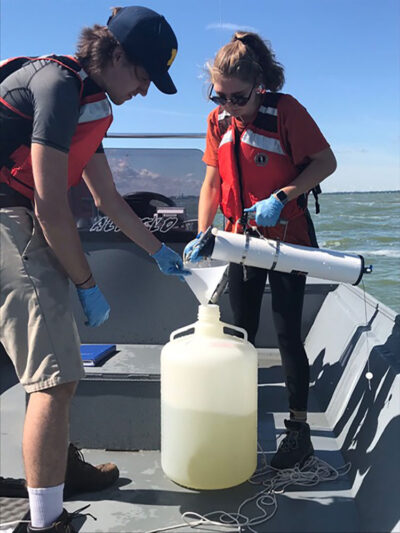 A photo of two students collecting water from Lake Erie