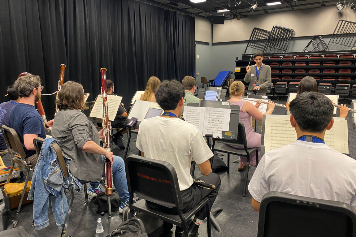 Photo of woodwinds players rehearsing and a conductor conducting.