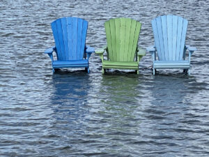 Three lawn chairs submerged in rising lake waters.