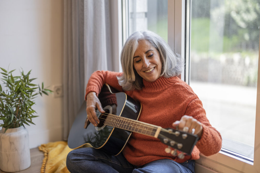 Senior woman tuning her guitar sitting on the couch in her living room. Image credit: Jose carlos Cerdeno, iStock