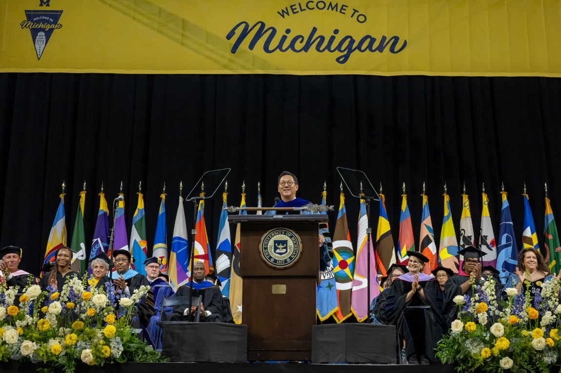 Photo of President Santa Ono behind a podium with university leaders seated behind him.
