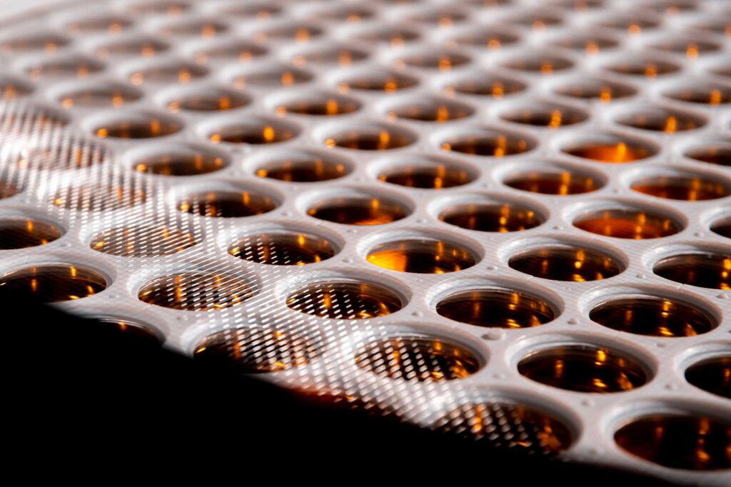 A close-up of the apertures of the photomultiplier tubes in the LZ detector. The tubes have shiny golden surfaces that are embedded in a large, flat, white holder.