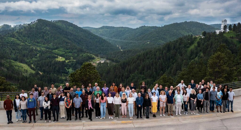 A group of dozens of researchers stands in front of rolling green hills in South Dakota.