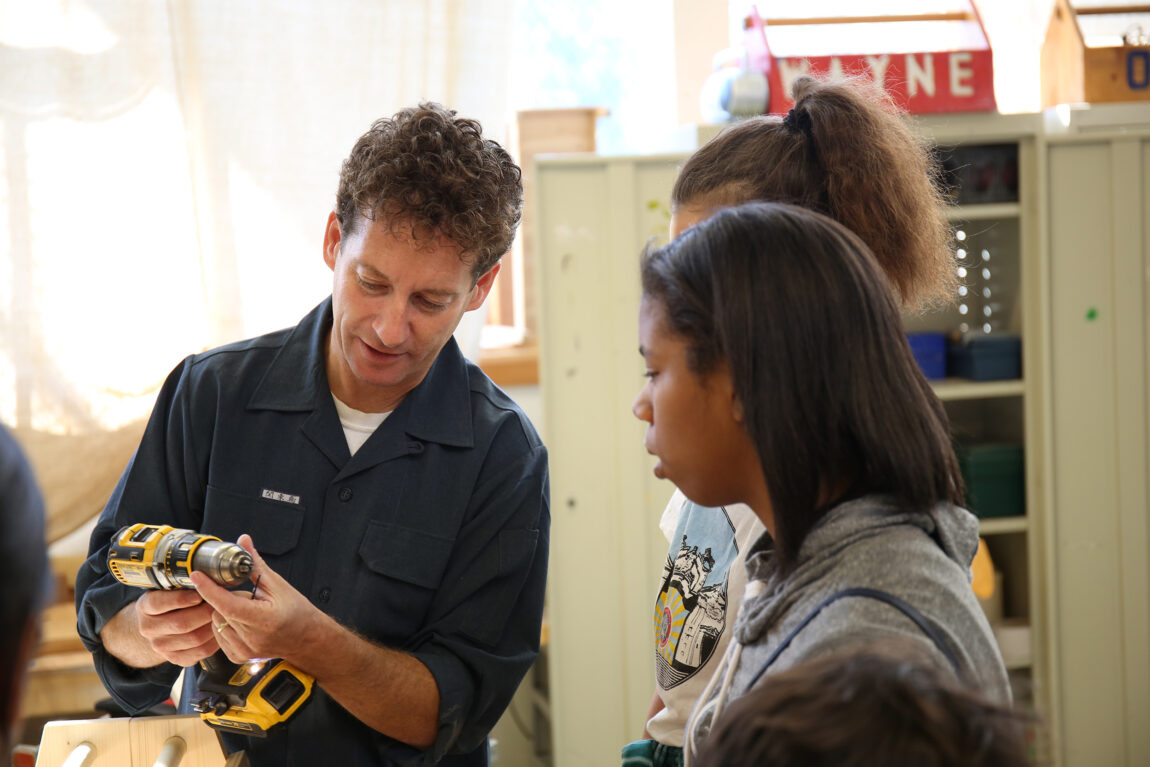 A photo of a man showing students how to operate a drill