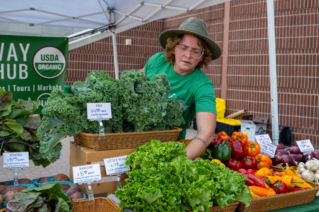 Photo of a woman arranging vegetables at a farm stand.