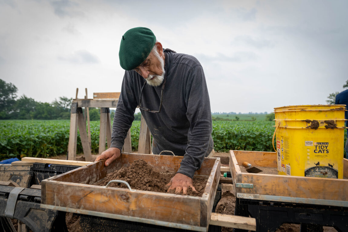A photo of a man sifting through dirt at an archaeological site