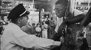 Black and white still from the documentary Ain't No Back to a Merry Go Round about the Glen Echo Amusement Park protest of 1960. Police officer confronts a Black man riding the carousel.