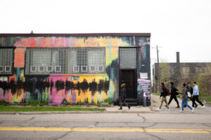 Students tour Detroit native and artist Scott Hocking’s studio and junkyard. The building is covered in colorful, flourescent paint.