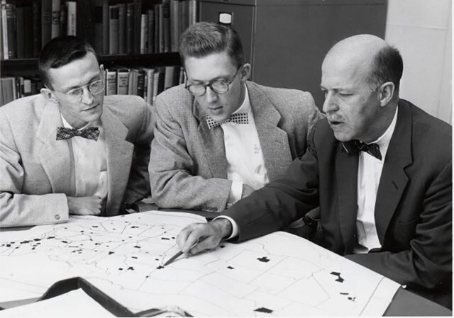 A photo of three men sitting at a table looking at a map of the United States