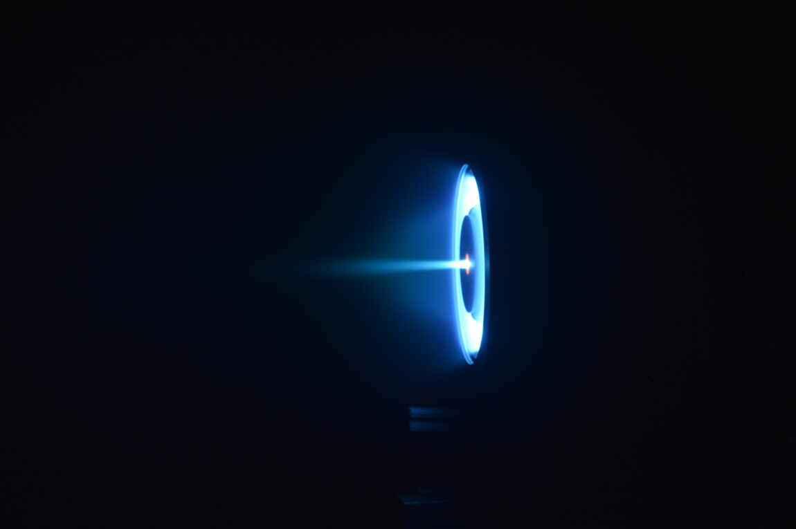 The thruster glows as a pale blue ring with a disk-shaped shadow in middle, and a blue ray streaking out from the center
