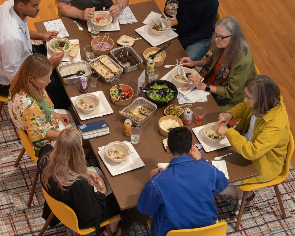 Photo of eight people seated around a table and eating a meal.