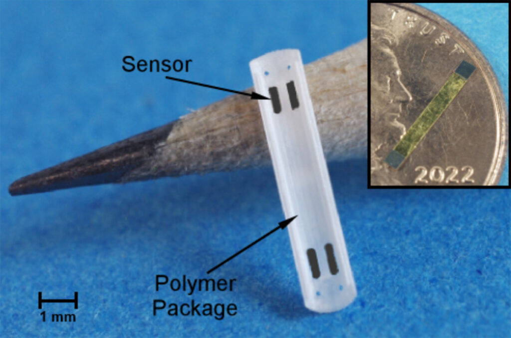 A ridged, rectangular, plastic piece labeled “polymer package” propped up against the tip of a standard pencil, about the same size. An arrow points to “sensor”: four small, film-like rectangles positioned at the plastic piece’s four corners. An inset shows the film-like sensor on a penny, less than half its diameter.