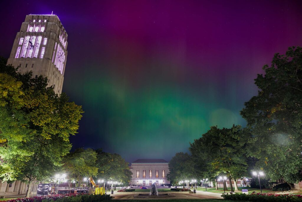 The northern lights fill the night sky above Ingalls Mall with vibrant green and purple hues.