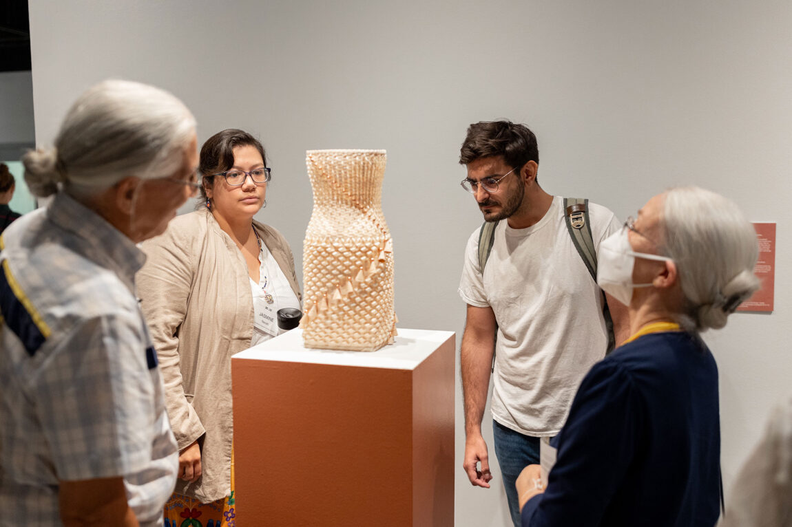 Photo of two men and two women looking at a woven basket on a pedestal