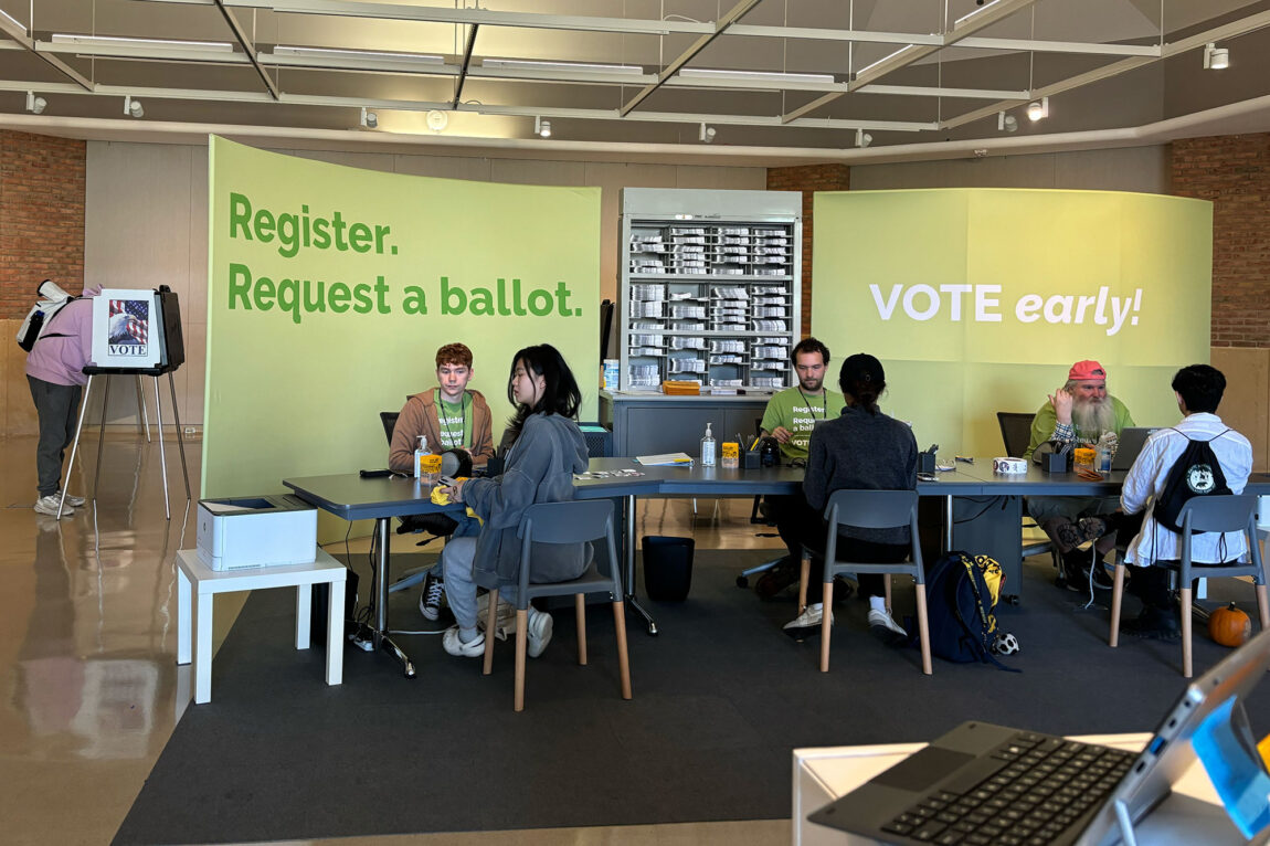 Photo of three students registering to vote while three staff members assist them.