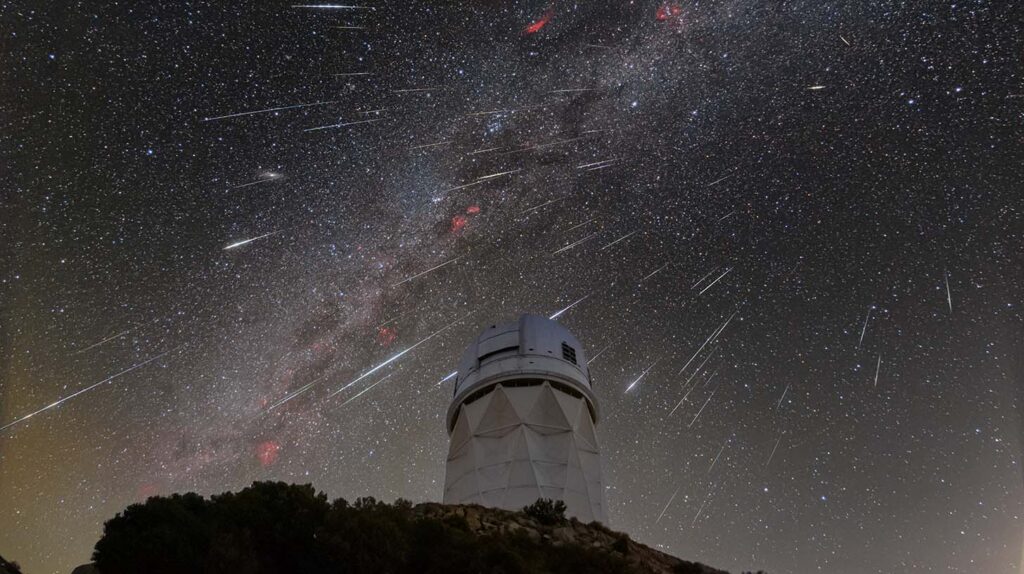 Meteors streak across a starry sky in the background, behind the white dome of the Nicholas U. Mayall 4-meter Telescope on Iolkam Du’ag, or Kitt Peak.
