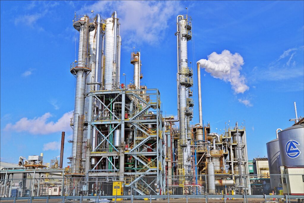 The metallic structures of an ethanol plant stand against a blue sky, with white