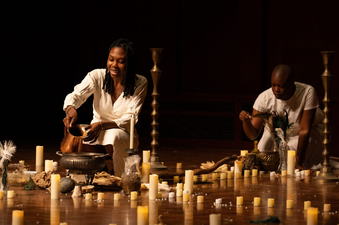 Photo of two women kneeling on stage surrounded by candles