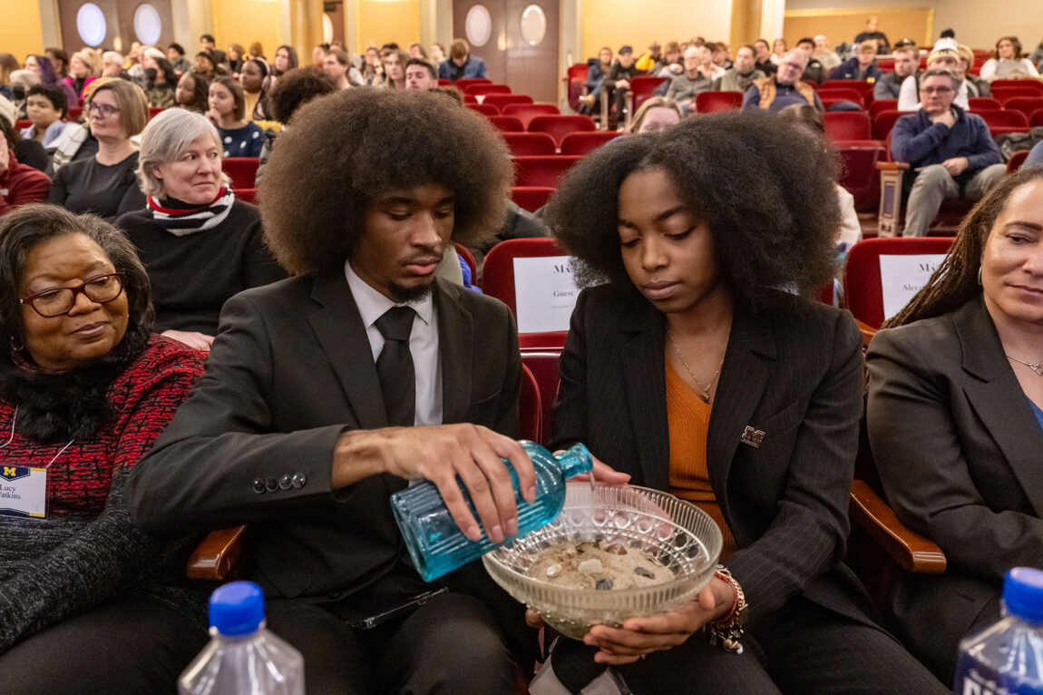 Photo of a man pouring water into a bowl of sand being held by a woman
